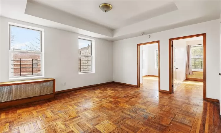 Empty room featuring parquet floors, radiator heating unit, and a raised ceiling