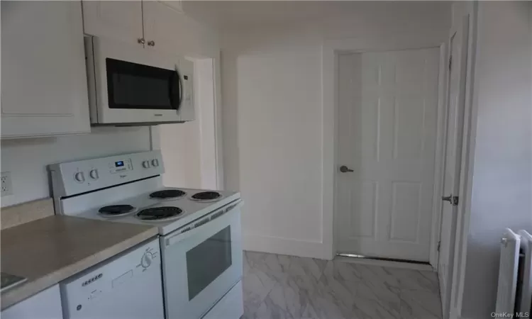 Kitchen with white appliances, white cabinets, radiator heating unit, and light tile floors