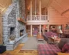 Living room featuring log walls, beamed ceiling, hardwood / wood-style floors, a stone fireplace, and high vaulted ceiling