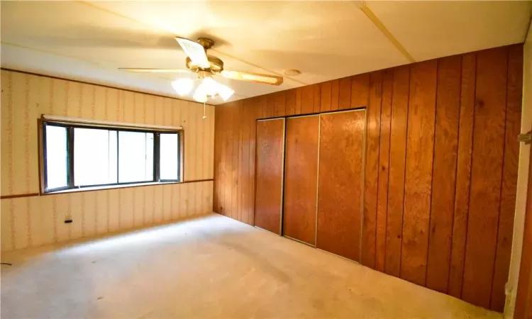 Unfurnished bedroom featuring a closet, wood walls, ceiling fan, and carpet flooring