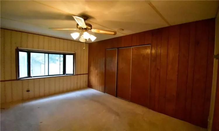 Unfurnished bedroom featuring a closet, carpet, ceiling fan, and wood walls