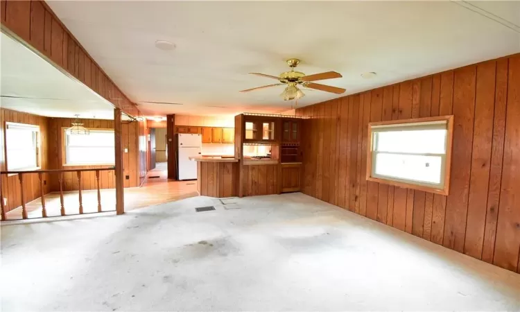 Unfurnished living room featuring wood walls, ceiling fan, light colored carpet, and plenty of natural light