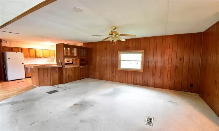 Unfurnished living room featuring wooden walls, ceiling fan, and light colored carpet