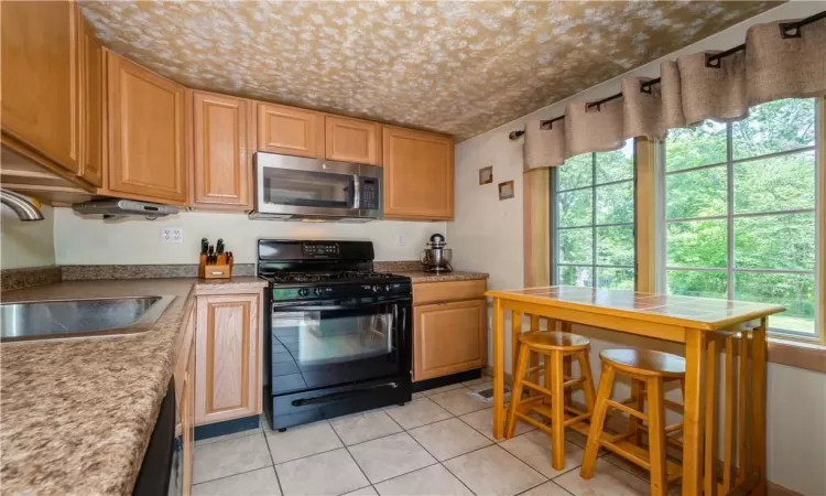 Kitchen featuring black gas range, sink, and light tile floors