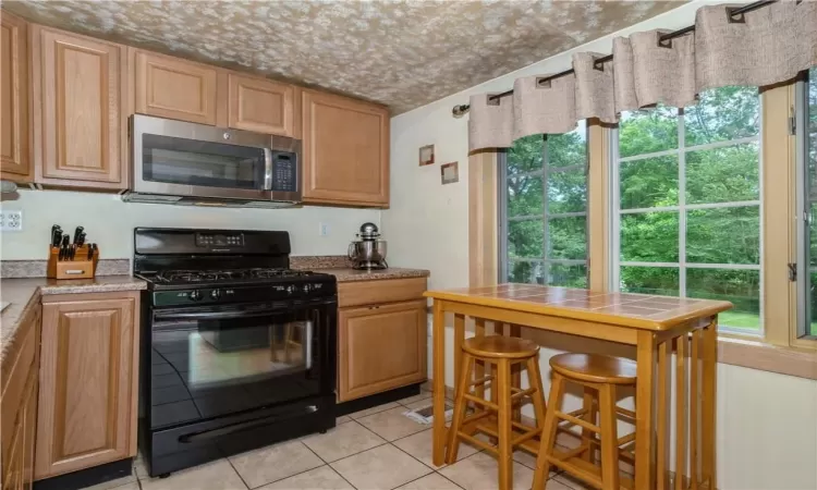 Kitchen with light stone countertops, black range with gas stovetop, and light tile flooring