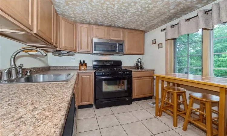 Kitchen featuring light tile floors, sink, a wealth of natural light, and black range with gas cooktop