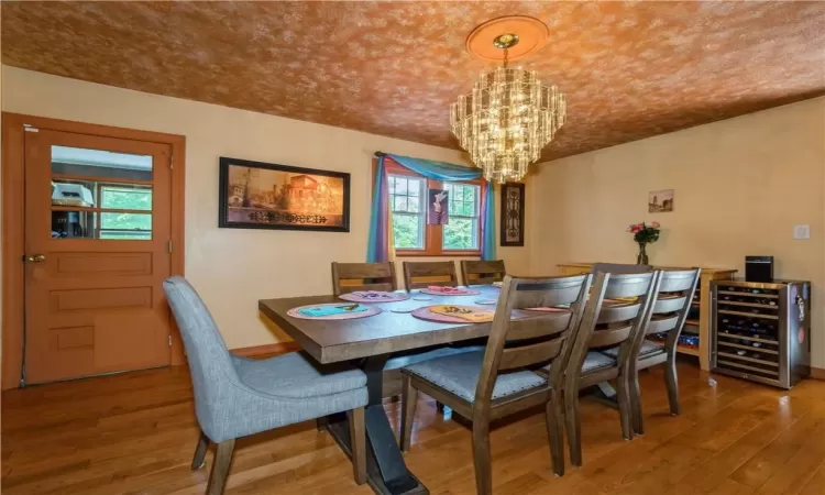 Dining space with a wealth of natural light, wood-type flooring, an inviting chandelier, and wine cooler