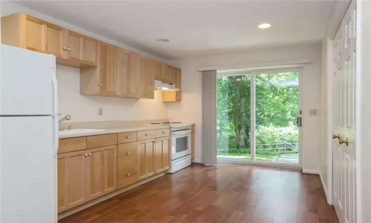 Kitchen with light brown cabinets, hardwood / wood-style floors, sink, and white appliances