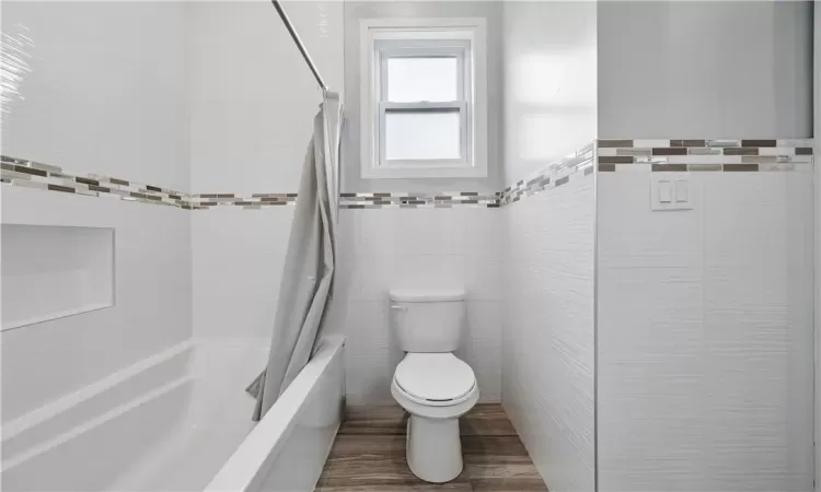 Bathroom with tile walls, shower / bathtub combination with curtain, and toilet