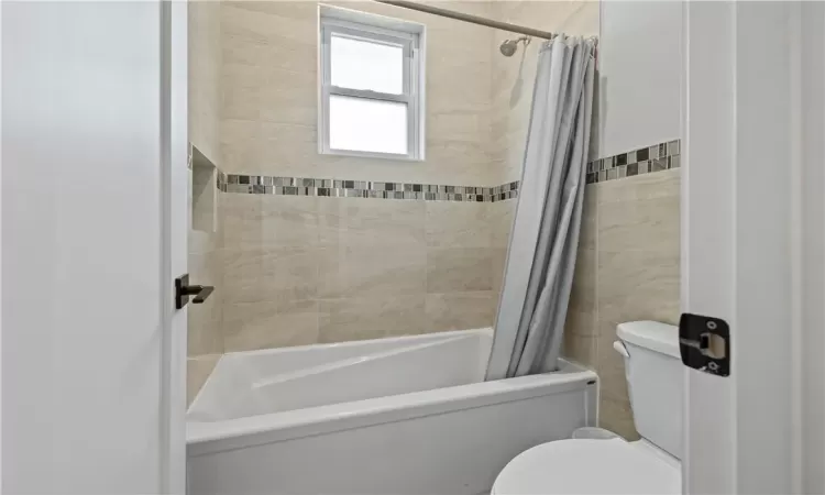 Bathroom featuring tile walls, toilet, and shower / tub combo with curtain