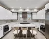 Kitchen featuring range hood, a kitchen island, appliances with stainless steel finishes, white cabinets, and a kitchen bar