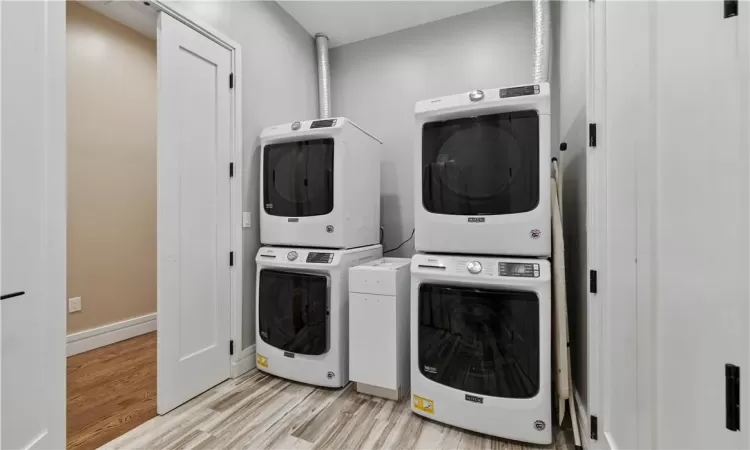 Washroom with stacked washing maching and dryer and light hardwood / wood-style flooring