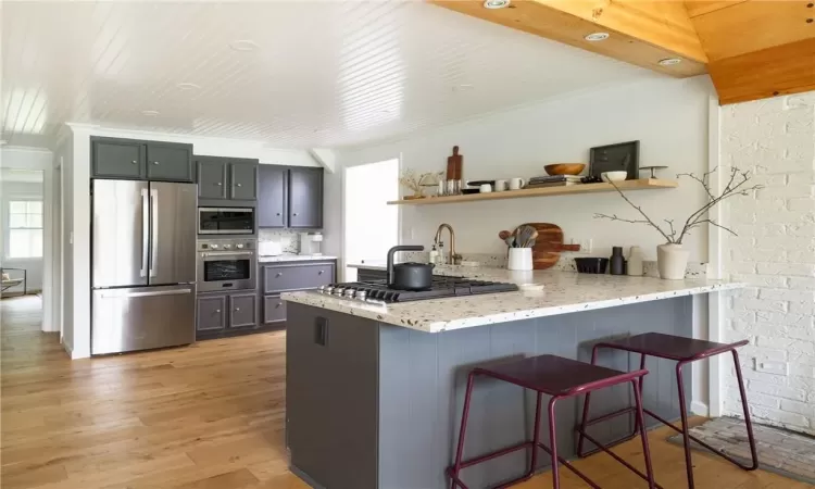 Kitchen with crown molding, kitchen peninsula, light wood-type flooring, light stone counters, and appliances with stainless steel finishes