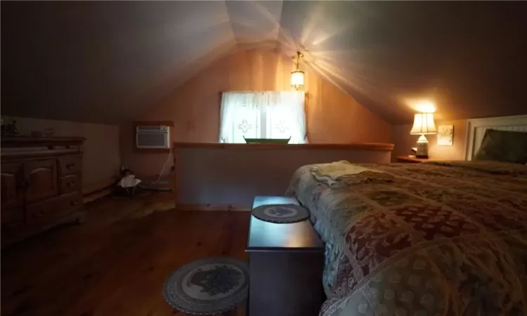 Bedroom featuring a wall unit AC, vaulted ceiling, and hardwood / wood-style flooring