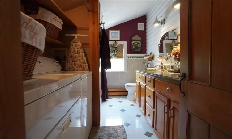 Bathroom featuring washer and clothes dryer, tile floors, vaulted ceiling, vanity, and toilet