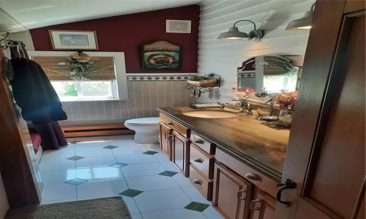 Bathroom featuring tile walls, toilet, vanity, and lofted ceiling