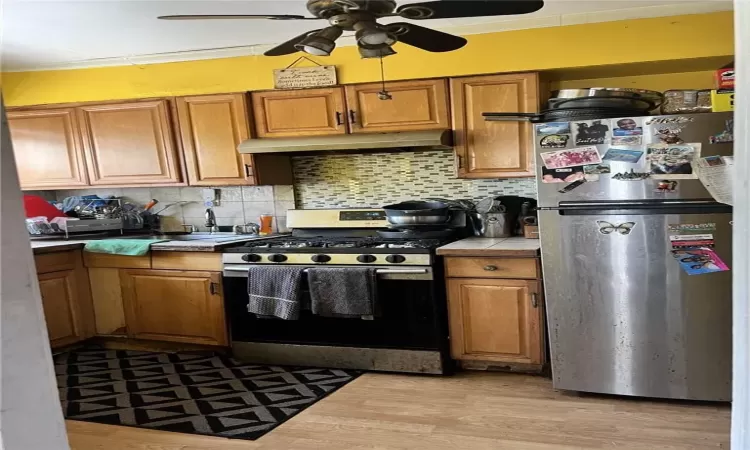 Kitchen featuring light hardwood / wood-style floors, backsplash, stainless steel refrigerator, gas range, and ceiling fan