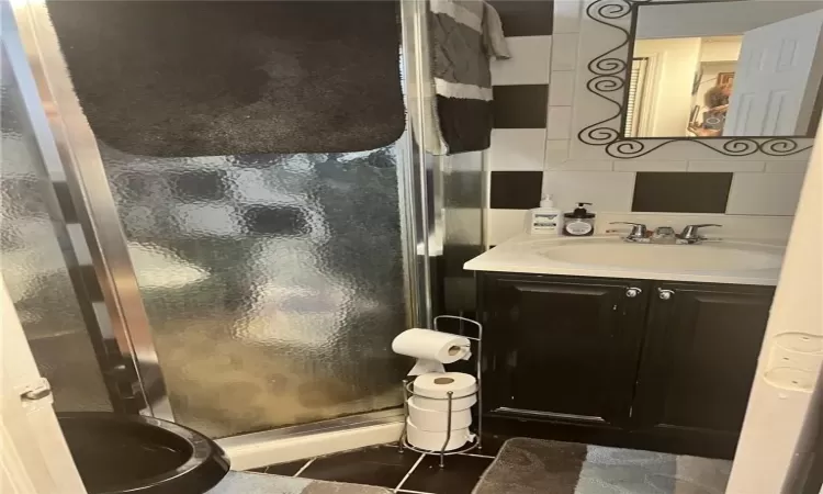 Bathroom featuring an enclosed shower, backsplash, tile flooring, and vanity