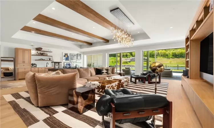 Living room featuring light hardwood / wood-style flooring, beam ceiling, a notable chandelier, a raised ceiling, and sink