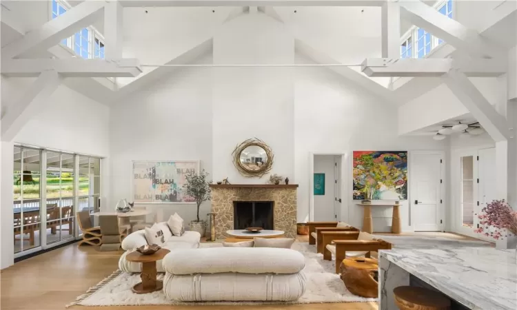 Living room featuring high vaulted ceiling, light wood-type flooring, a fireplace, and a healthy amount of sunlight