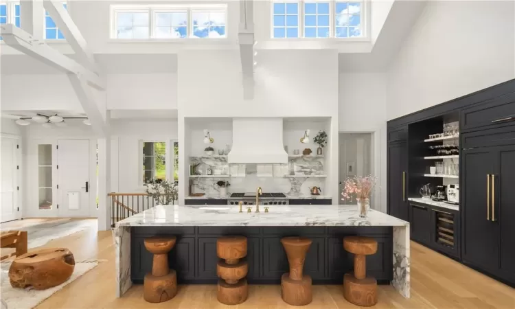 Kitchen with high vaulted ceiling, a kitchen island with sink, light hardwood / wood-style floors, and custom exhaust hood