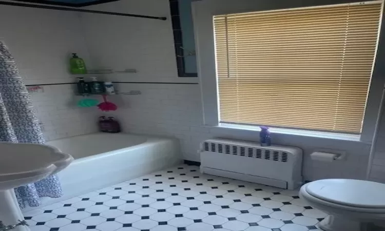 Bathroom with tile floors, tile walls, toilet, and radiator