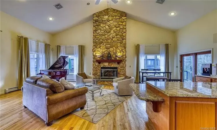 Living room with a healthy amount of sunlight, a stone fireplace, high vaulted ceiling, and light wood-type flooring