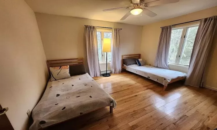 Bedroom featuring light hardwood / wood-style floors, baseboard heating, and ceiling fan