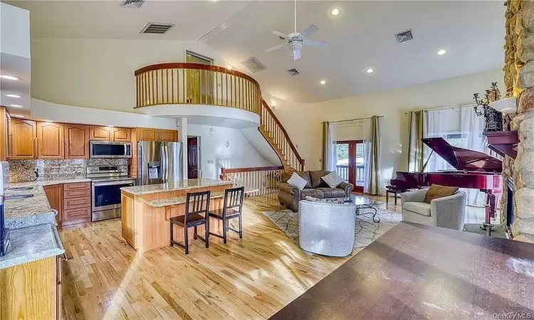 Kitchen featuring a center island, light hardwood / wood-style flooring, stainless steel appliances, high vaulted ceiling, and a kitchen bar