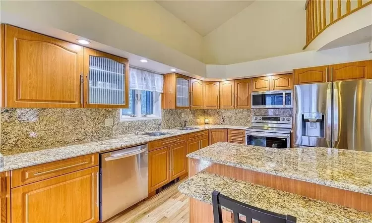 Kitchen with light stone counters, appliances with stainless steel finishes, tasteful backsplash, and light hardwood / wood-style flooring