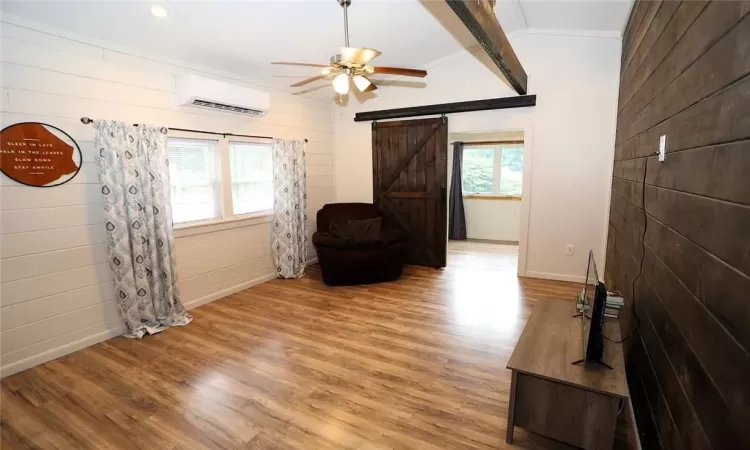 Living room featuring a mini-split unit, ceiling fan, wood-style floors, a barn door for access to second bedroom