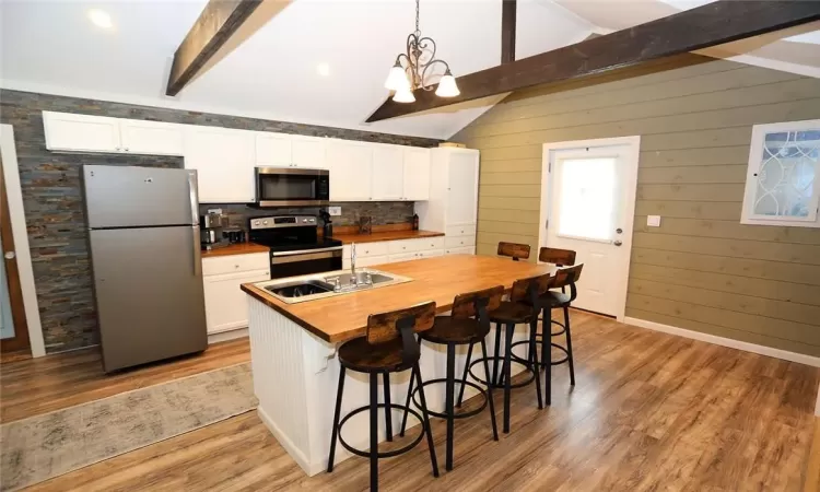 Kitchen featuring butcher block countertops, an island with sink, wood-type flooring, white cabinets, and appliances with stainless steel finishes