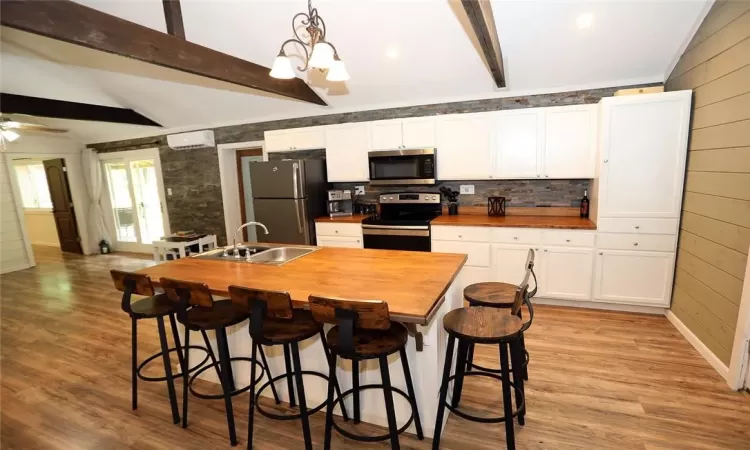 Kitchen featuring lofted ceiling with beams, hanging light fixtures, sink, white cabinetry, and appliances with stainless steel finishes