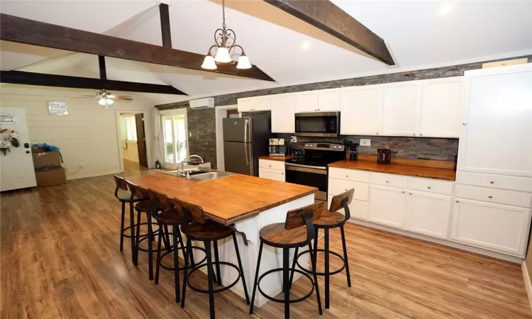 Kitchen featuring stainless steel appliances, butcher block countertops, ceiling fan with notable chandelier, and pendant lighting