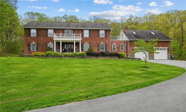 Colonial inspired home featuring a garage, a front lawn, and a balcony