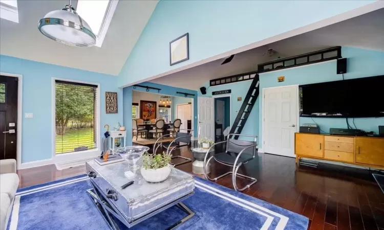 Living room with a skylight, high vaulted ceiling, and dark wood-type flooring