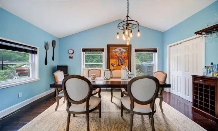 Dining space featuring dark hardwood / wood-style flooring, an inviting chandelier, a healthy amount of sunlight, and lofted ceiling