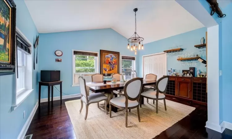 Dining area with an inviting chandelier, lofted ceiling, and dark wood-type flooring