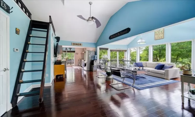 Living room with dark hardwood / wood-style flooring, a wealth of natural light, ceiling fan, and high vaulted ceiling