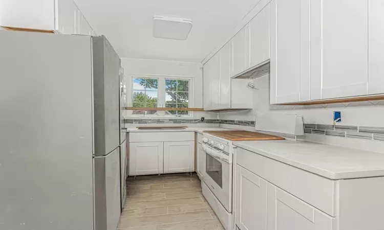 Kitchen with white cabinets, range, oven, decorative backsplash, and refrigerator