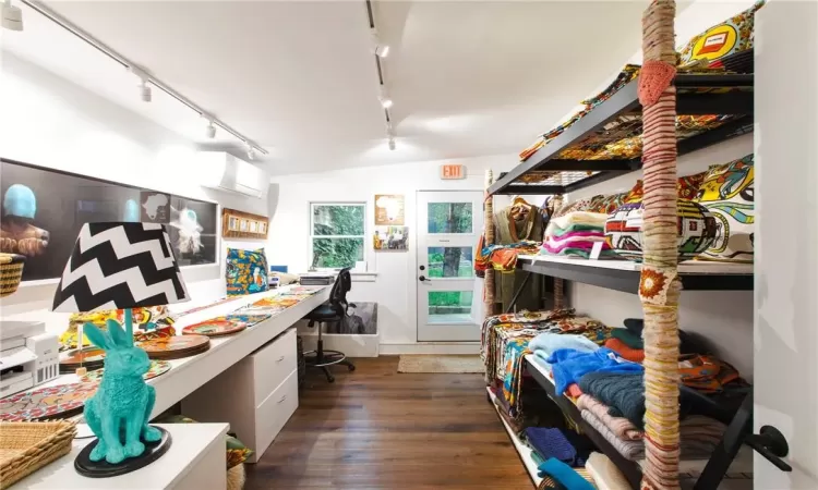 Shop/Retail featuring dark hardwood / wood-style floors, track lighting, built in desk, vaulted ceiling, and a wall mounted air conditioner