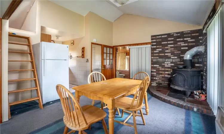 Dining area featuring dark carpet, lofted ceiling, and a wood stove