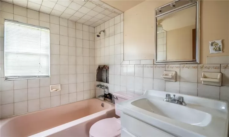 Full bathroom featuring vanity, tile walls, tiled shower / bath combo, and toilet