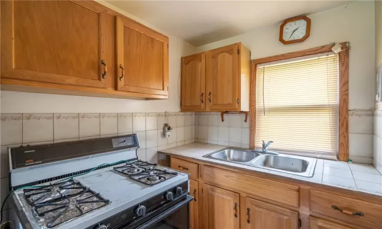 Kitchen featuring backsplash, tile counters, white gas stove, and sink