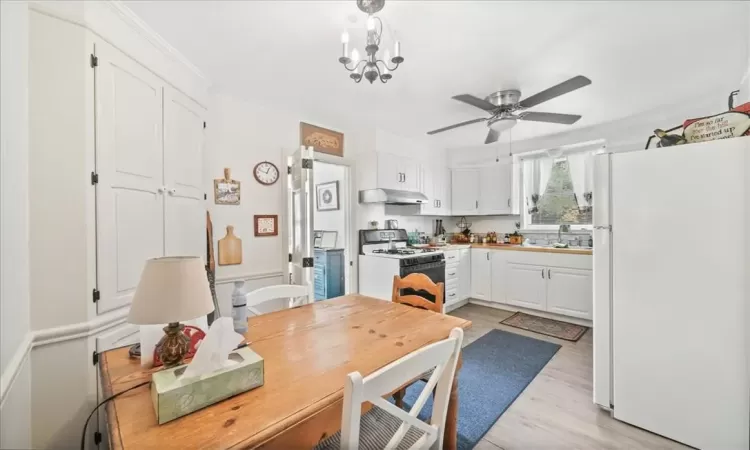 Kitchen featuring white appliances, sink, ceiling fan with notable chandelier, light hardwood / wood-style floors, and white cabinets