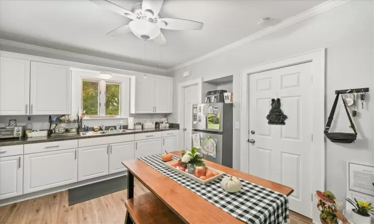 Kitchen featuring ornamental molding, white cabinetry, light hardwood / wood-style floors, ceiling fan, and stainless steel refrigerator