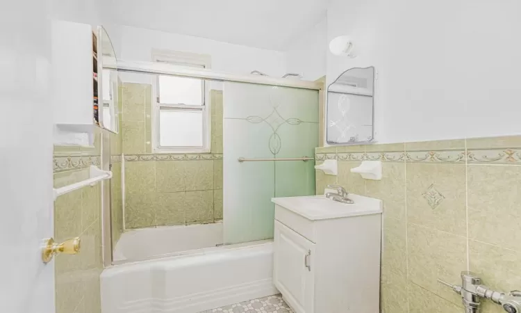 Bathroom featuring vanity, tile walls, and bath / shower combo with glass door