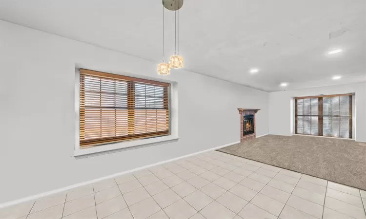 Unfurnished living room with light colored carpet, a brick fireplace, and a notable chandelier