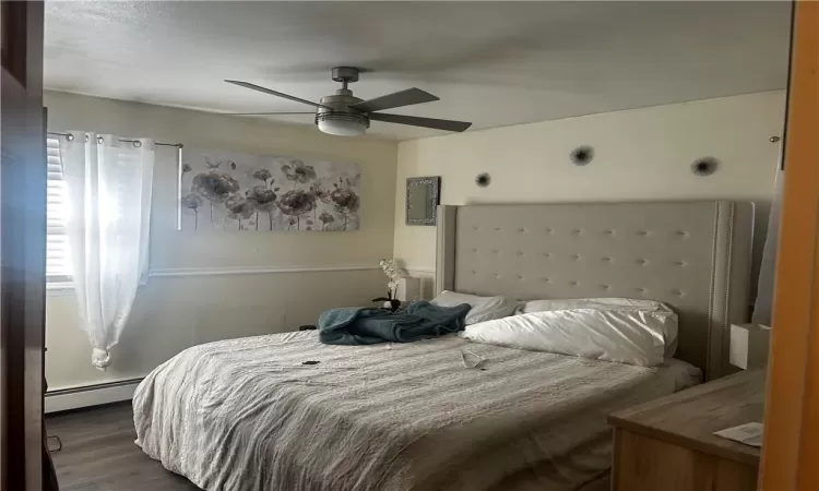 Bedroom featuring a baseboard heating unit, dark hardwood / wood-style floors, and ceiling fan