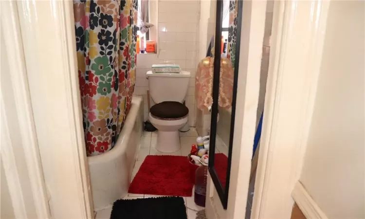 Bathroom featuring tile walls, tile patterned floors, shower / bath combo with shower curtain, and toilet